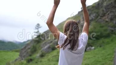 站在山顶上的漂亮女孩正在跳跃和举手。 慢动作